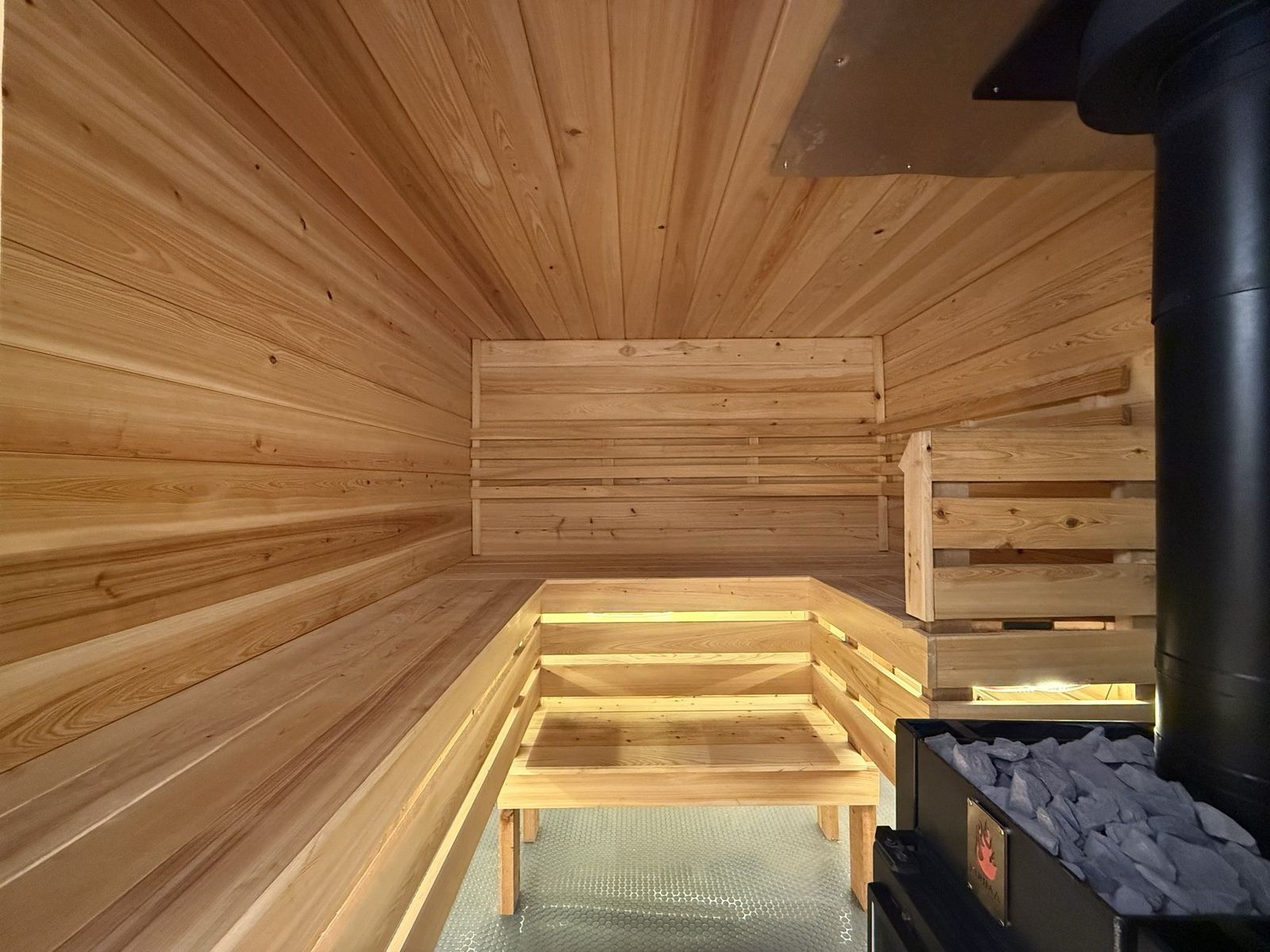Wide view of the cedar sauna interior with tiered benches and the Kuuma wood stove